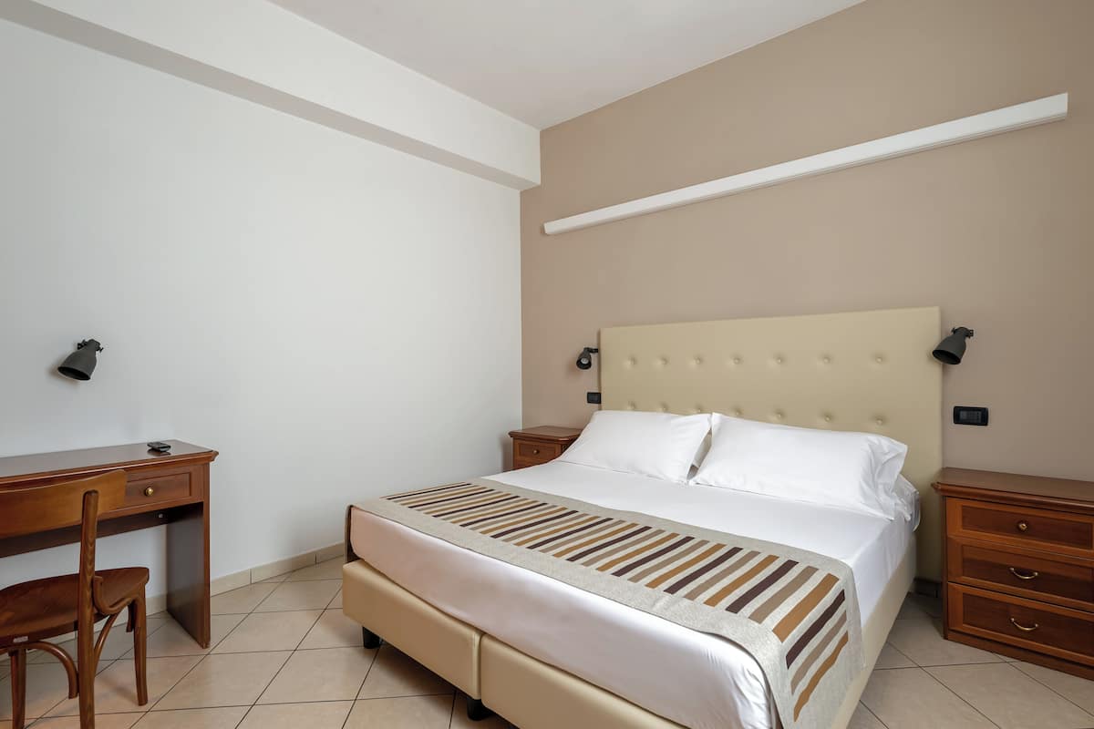 A bedroom with a bed, a desk, a chair, and a nightstand.