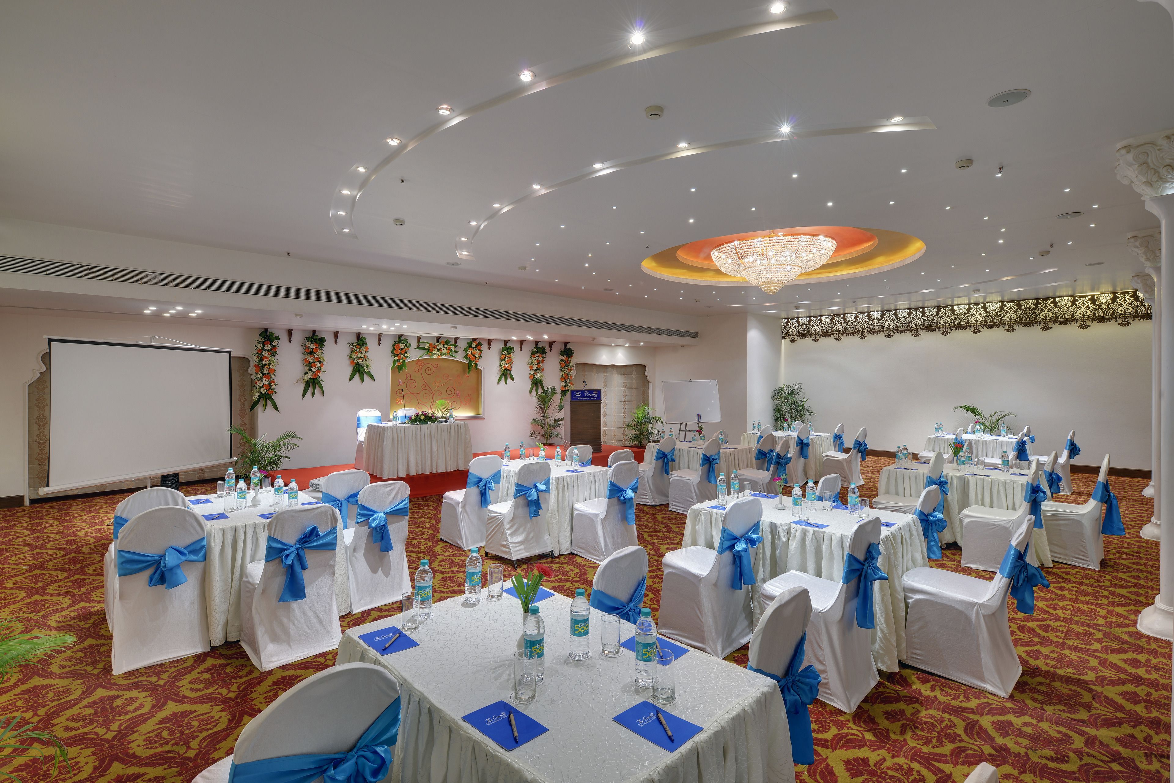 Un salón de banquetes con mesas redondas, manteles blancos y fajas azules.