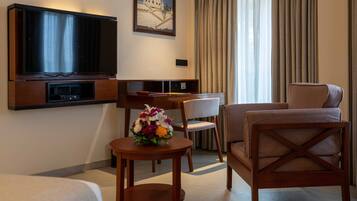A hotel room with a TV, a desk, a chair, a sofa, and a small table with a flower arrangement.