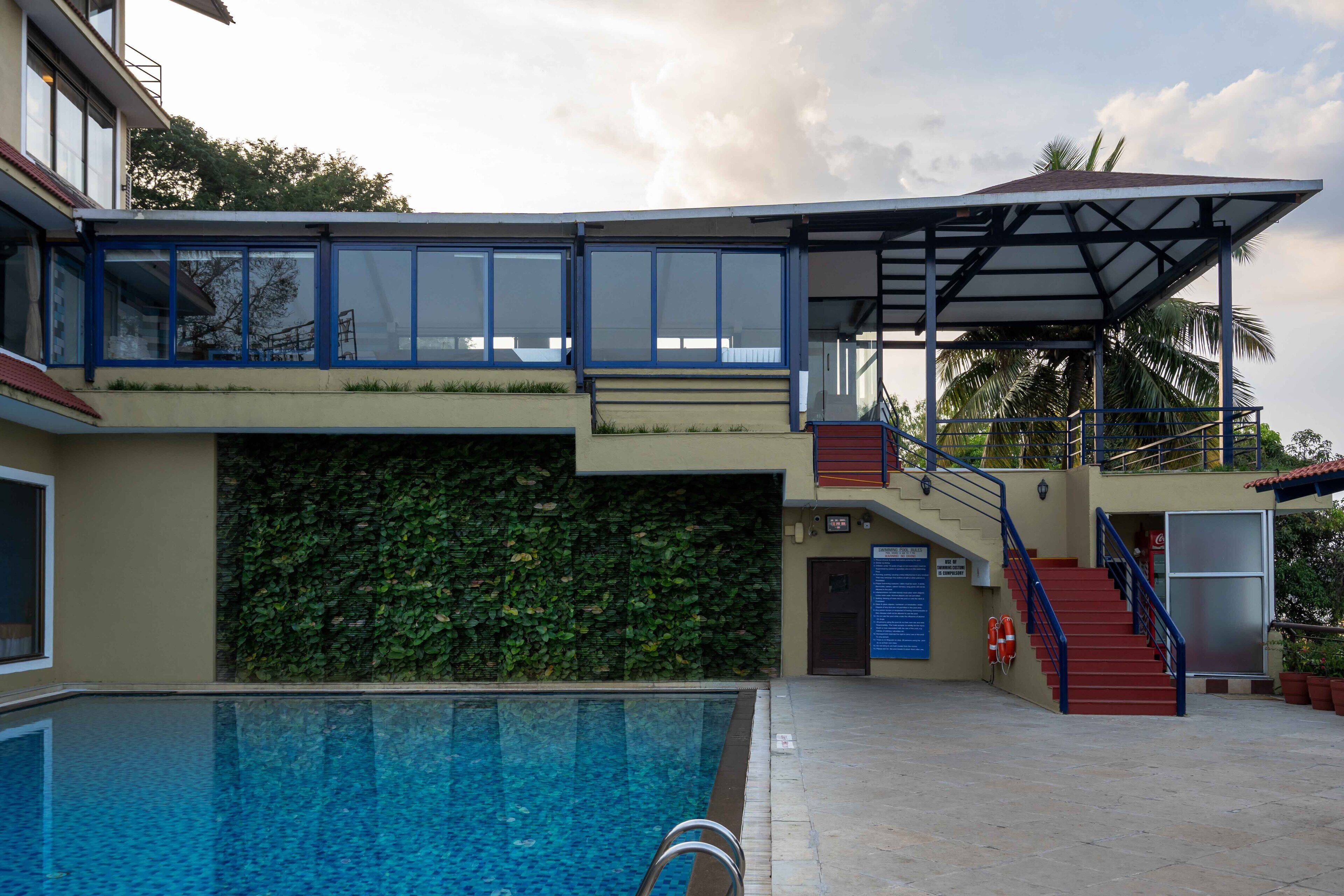 Ein Pool mit Glasboden, ein überdachter Bereich mit Treppe sowie ein Gebäude mit grüner Wand und blauer Brüstung.