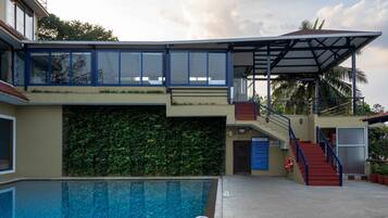 Ein Pool mit Glasboden, ein überdachter Bereich mit Treppe sowie ein Gebäude mit grüner Wand und blauer Brüstung.