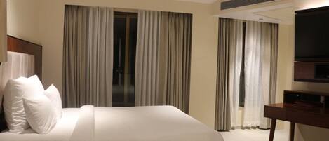 Una habitación de hotel con una cama grande, un escritorio con televisor de pantalla plana y dos ventanas con cortinas.