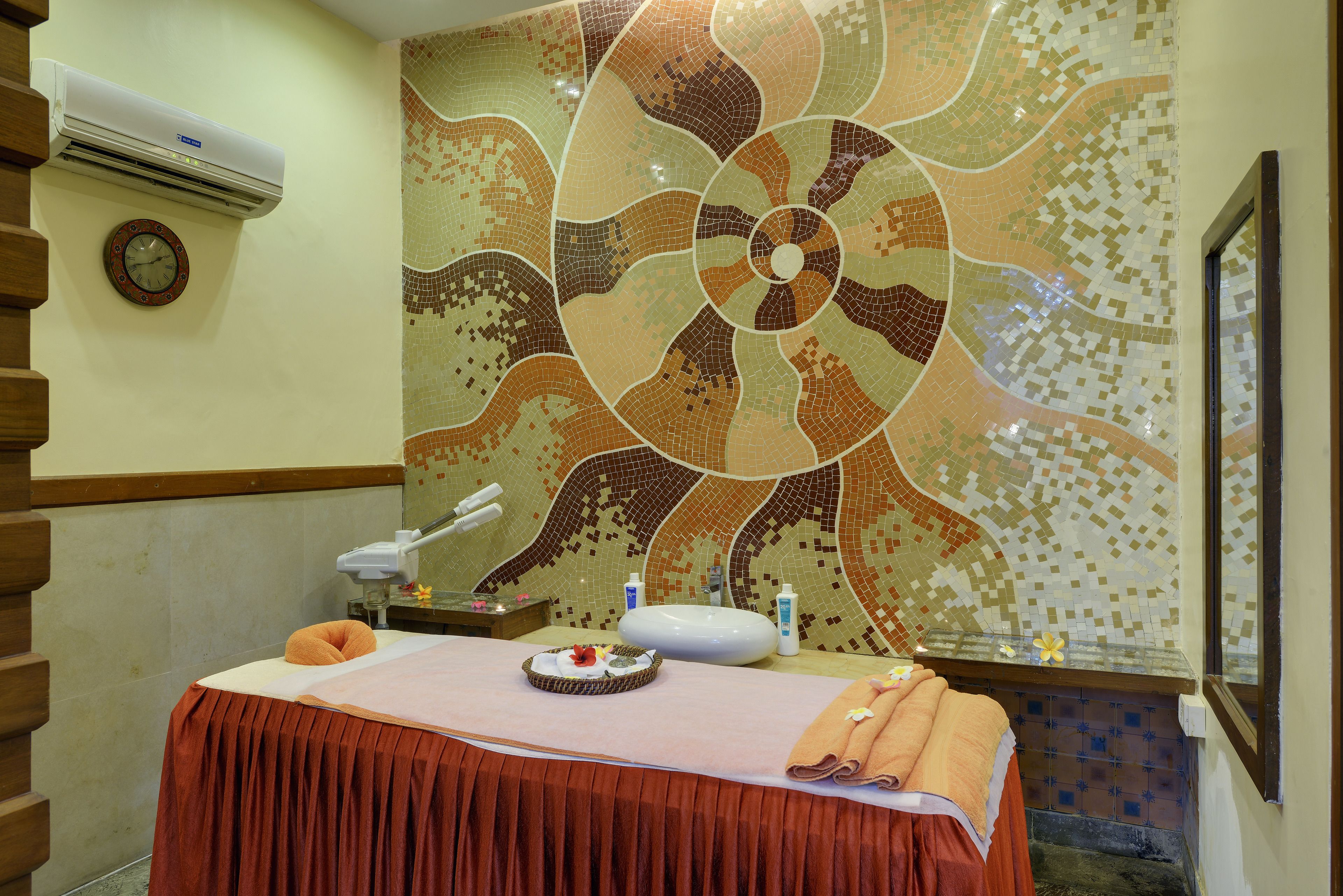 Un cuarto de spa con una camilla de masaje, un reloj y una pared decorativa con mosaicos.