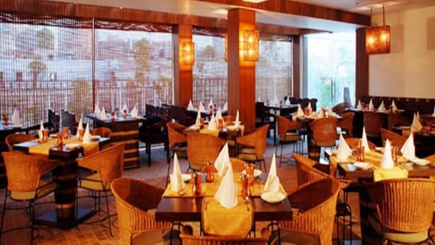 A spacious restaurant with multiple tables and chairs, large windows, and warm lighting. - Hotel Palace Heights (New Delhi)