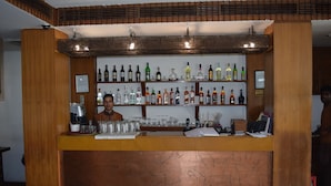 A bar area with a wooden counter, shelves of various liquor bottles, glasses, and a cash register. - Hotel Palace Heights (New Delhi)