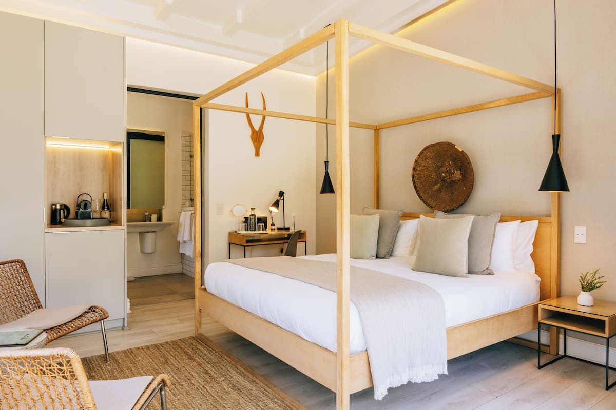 A four-poster bed with a wooden frame, a bedside table with a lamp, a chair, and a small plant on a nightstand.