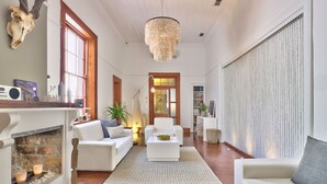 A spacious living room with a fireplace, white sofas, a chandelier, and a large window. - Cape Diem Lodge  (Cape Town)