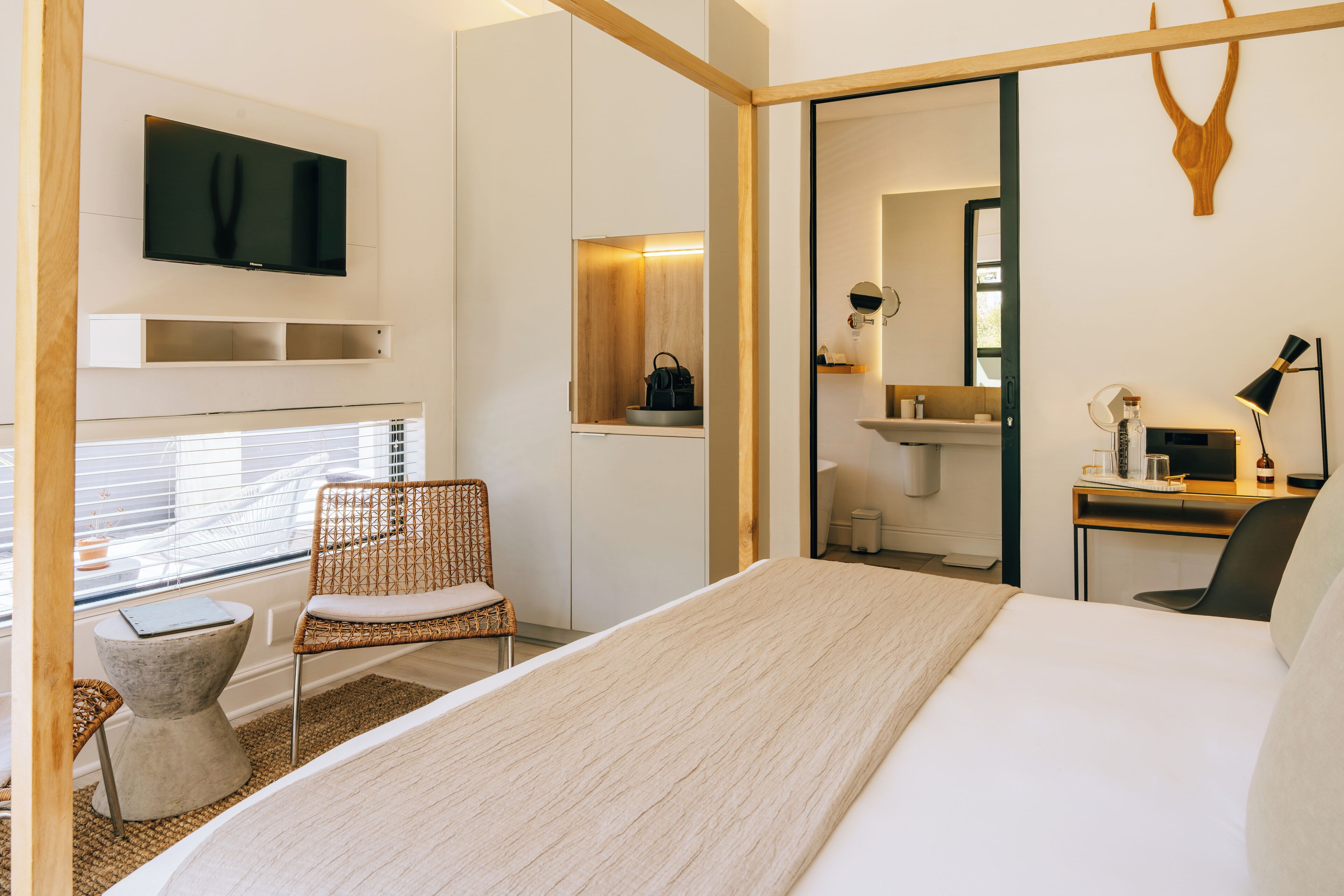A modern hotel room with a bed, a TV, a desk, and a bathroom visible through an open door.