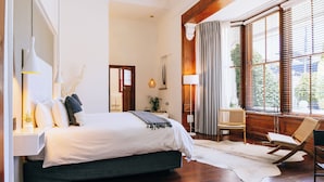 A bedroom with a bed, bedside lamps, a window with blinds, a chair, and a rug. - Cape Diem Lodge  (Cape Town)