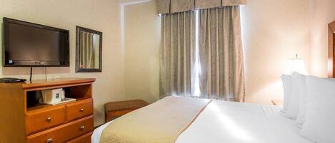 Une chambre d’hôtel avec un lit, une télévision, une commode en bois, une chaise et une fenêtre avec des rideaux.