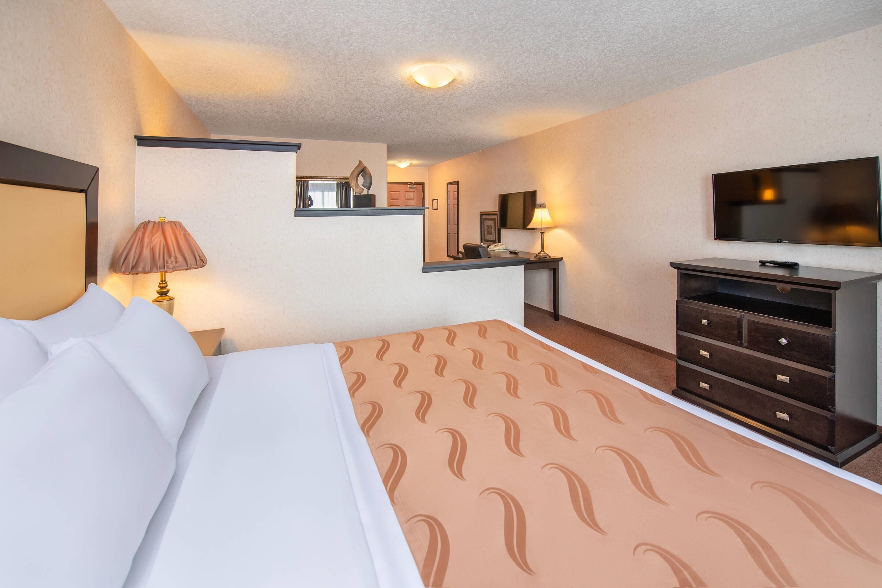 Una habitación de hotel con una cama, un aparador, un televisor y un escritorio con una lámpara.