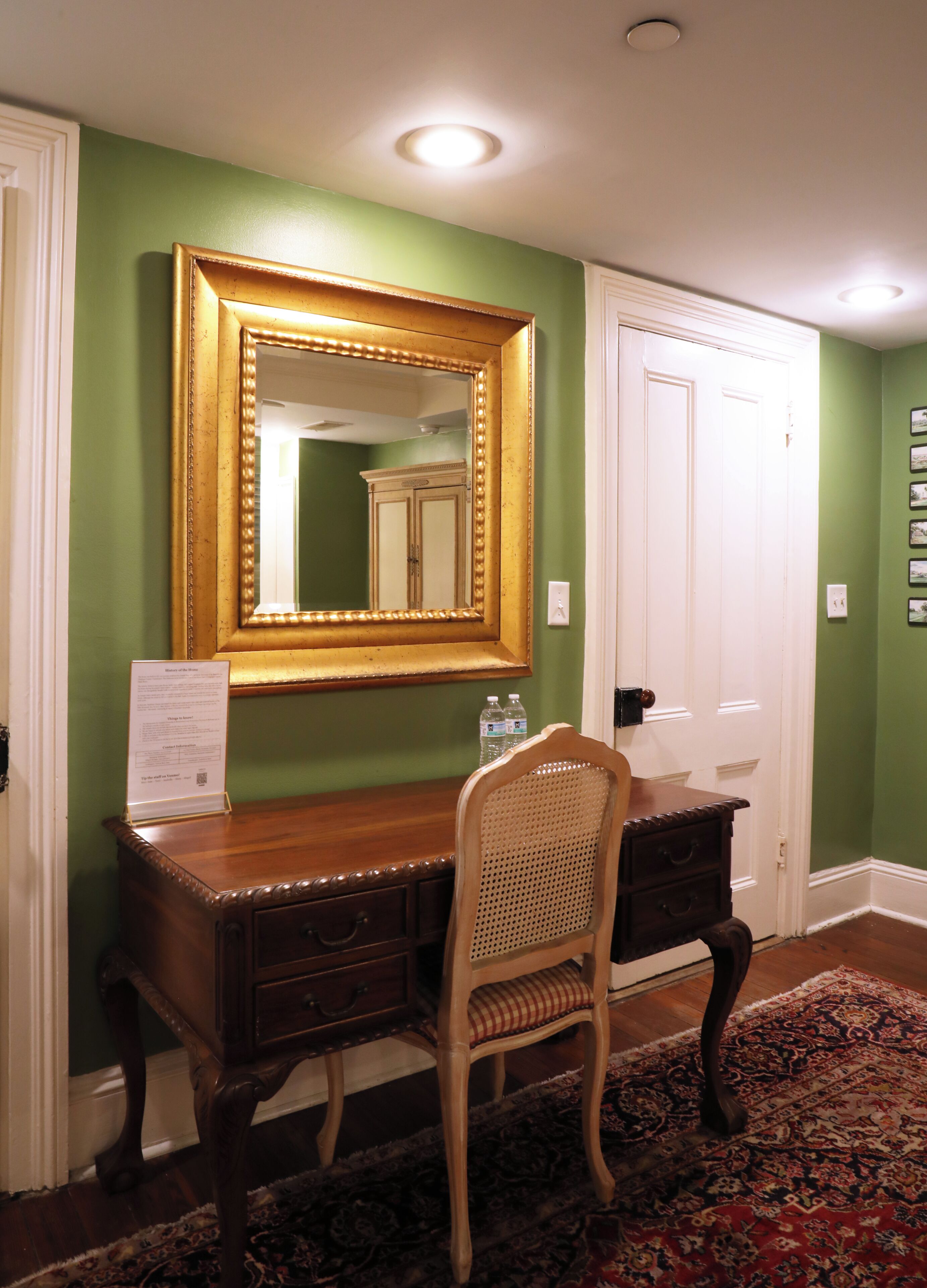 A room with a wooden desk, a chair, a large mirror, and a door.