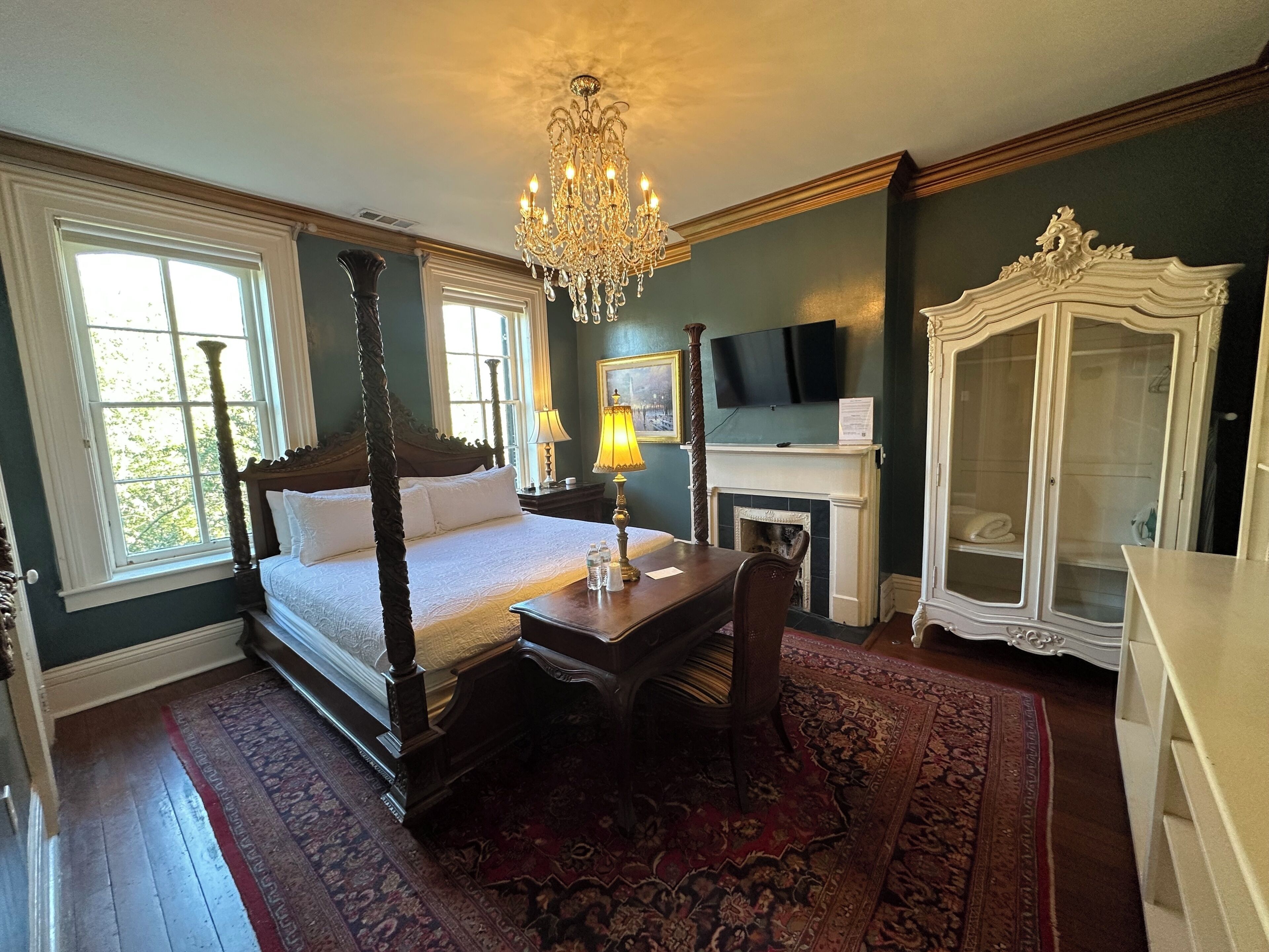 A four-poster bed, a chandelier, a fireplace, a television, and a cabinet.