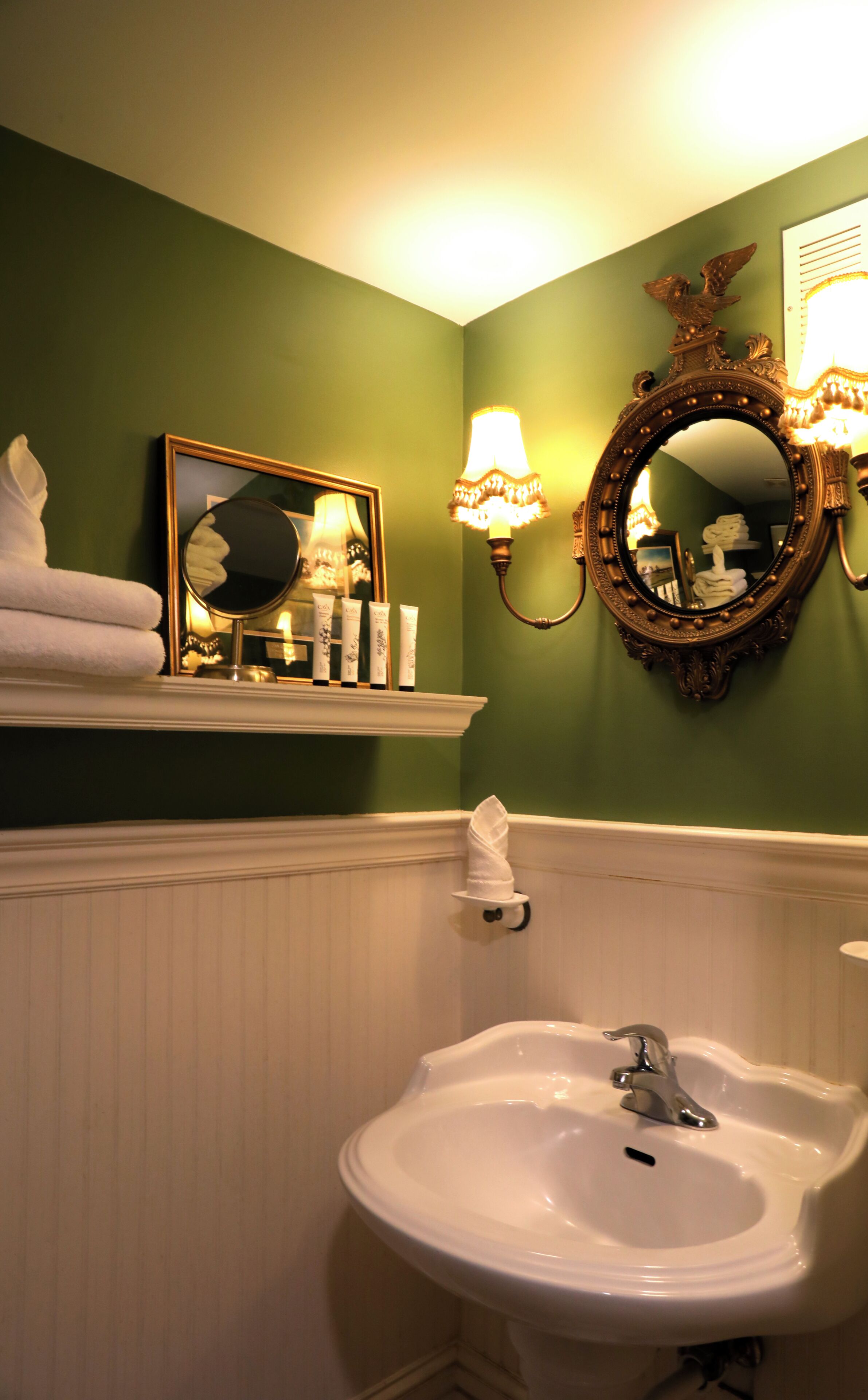A bathroom with a white sink, a mirror, and a shelf with toiletries.