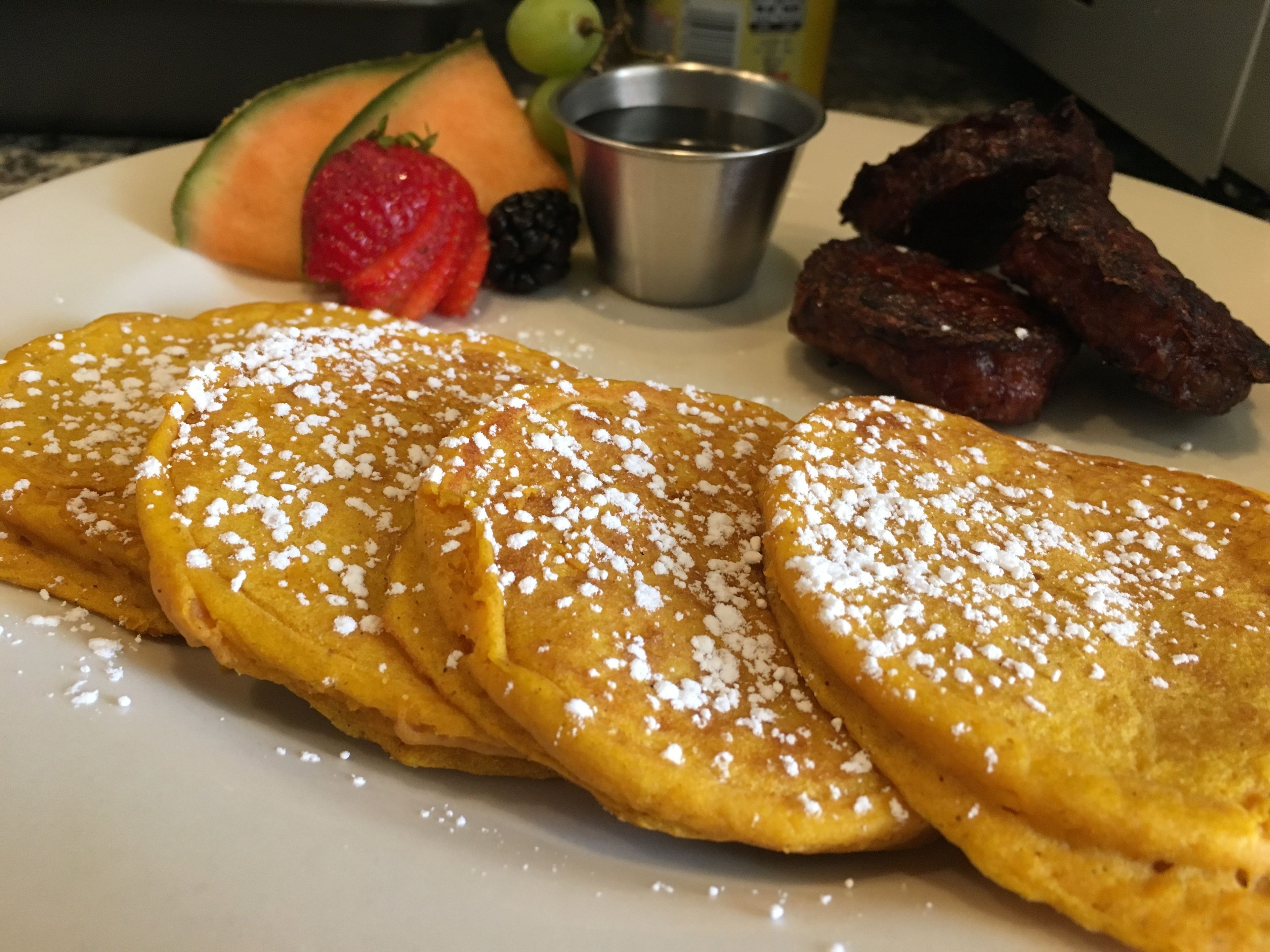 A plate with pancakes, fruit, and meat.