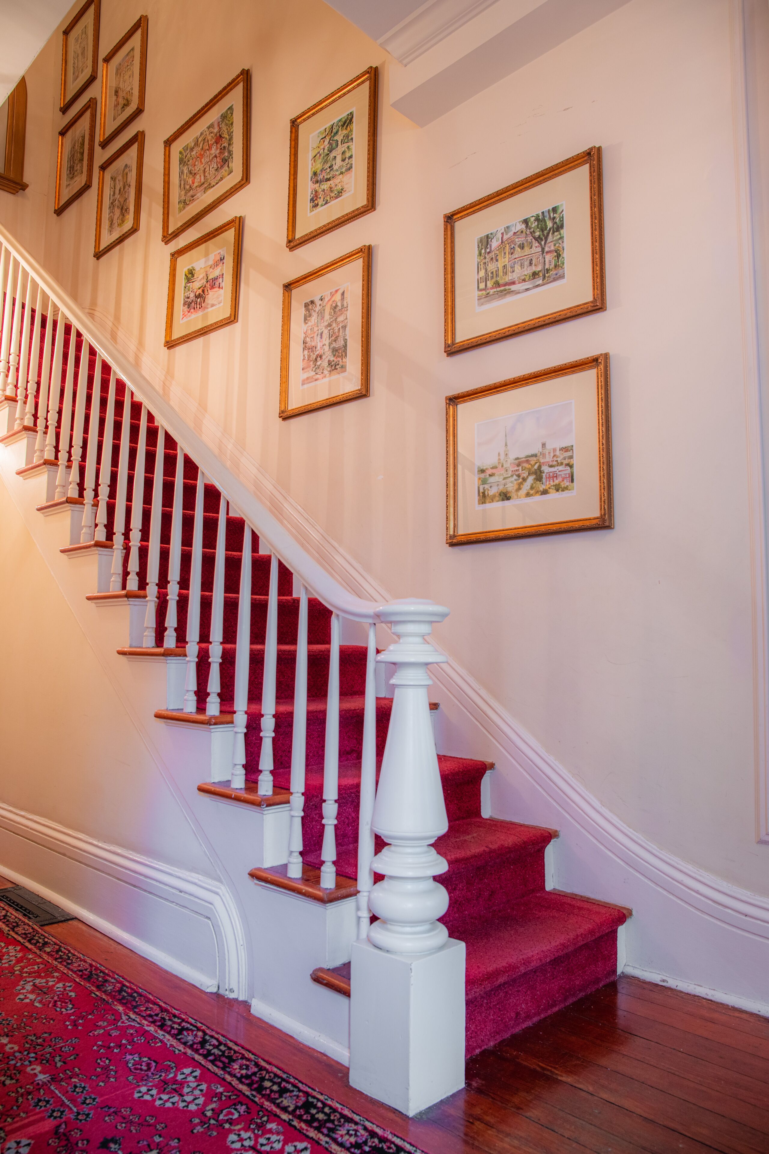 A staircase with red carpeted steps, white balusters, and a red carpet at the bottom.