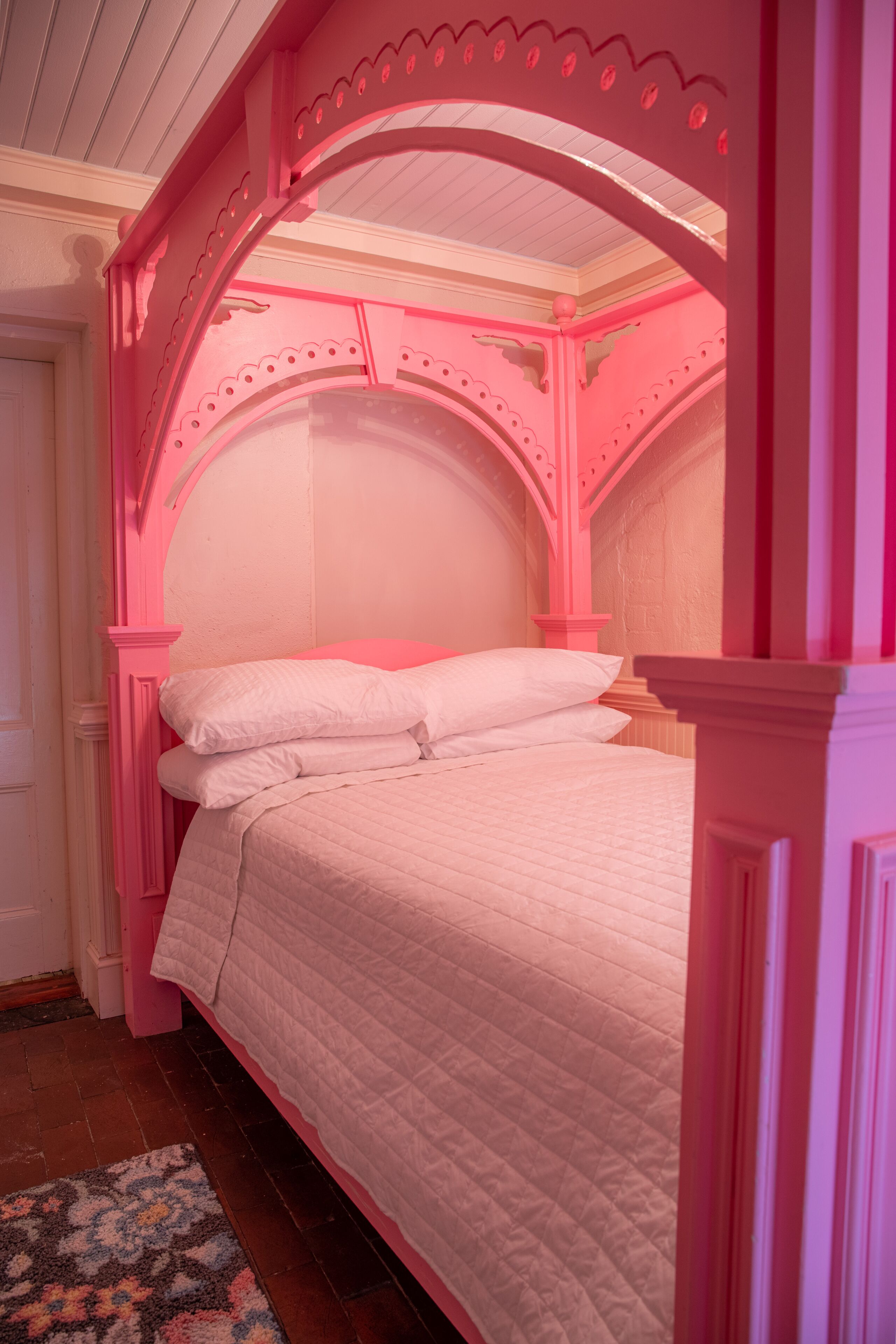 A pink-themed bedroom with a bed, pillows, and a patterned rug.