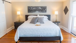 A neatly arranged bedroom with a large bed, two bedside tables, a chandelier, and a framed artwork on the wall.