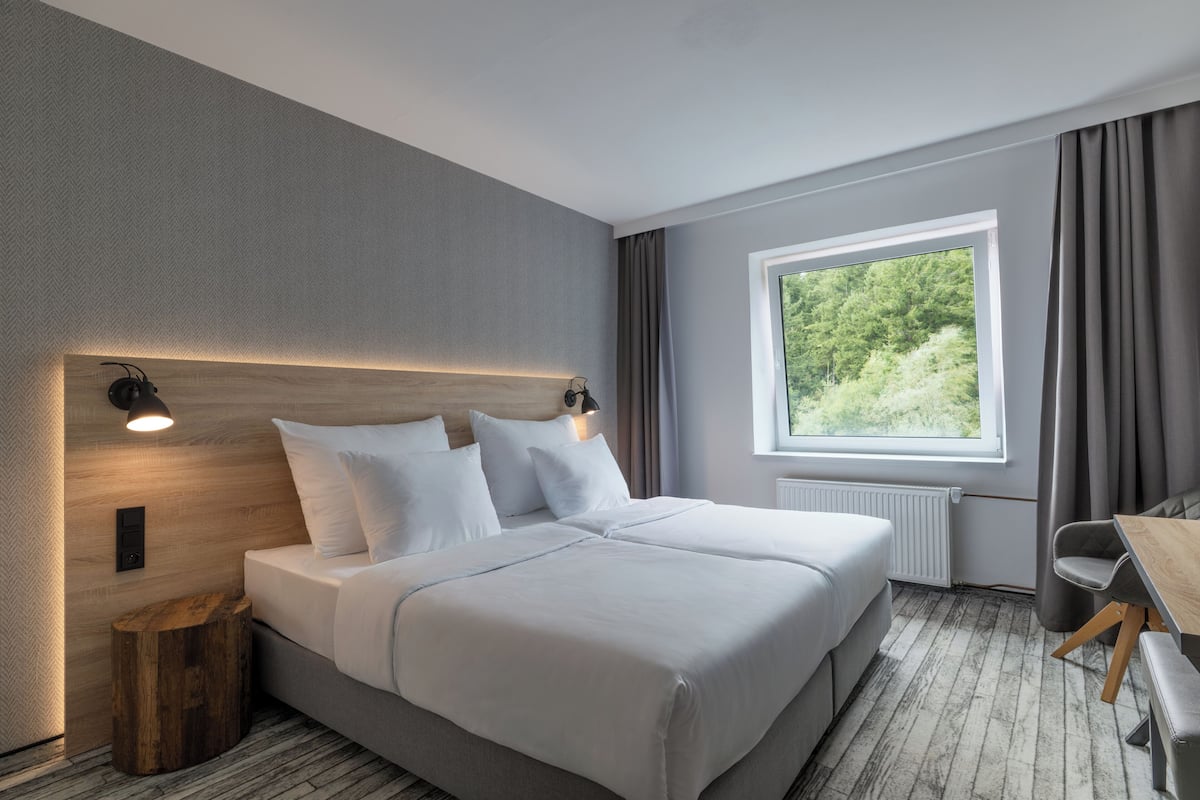 Habitación de hotel moderna con una cama grande, un escritorio y una ventana con vistas a zonas verdes.