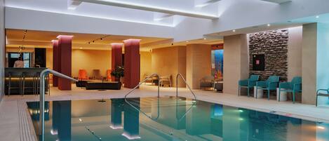 Area piscina interna moderna con acqua cristallina, zone relax e reception.