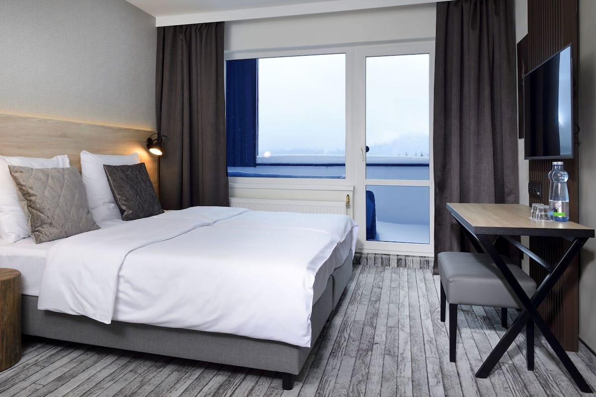 Una habitación de hotel con cama, escritorio, silla, televisor y vistas al exterior.
