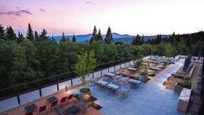 Un patio al aire libre con mesas y sillas, rodeado de árboles y vistas a un cuerpo de agua.