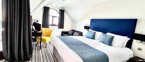 A modern hotel room with a large bed, a desk, a chair, and a view of the city.