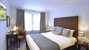 Hotelkamer met een groot bed, een bureau met stoel, een lamp en uitzicht op het omliggende landschap door het raam.