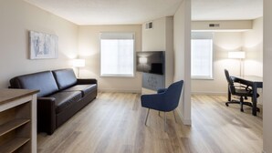 Una sala de estar moderna con un sofá, un televisor, un sillón azul y un comedor con mesa y sillas.