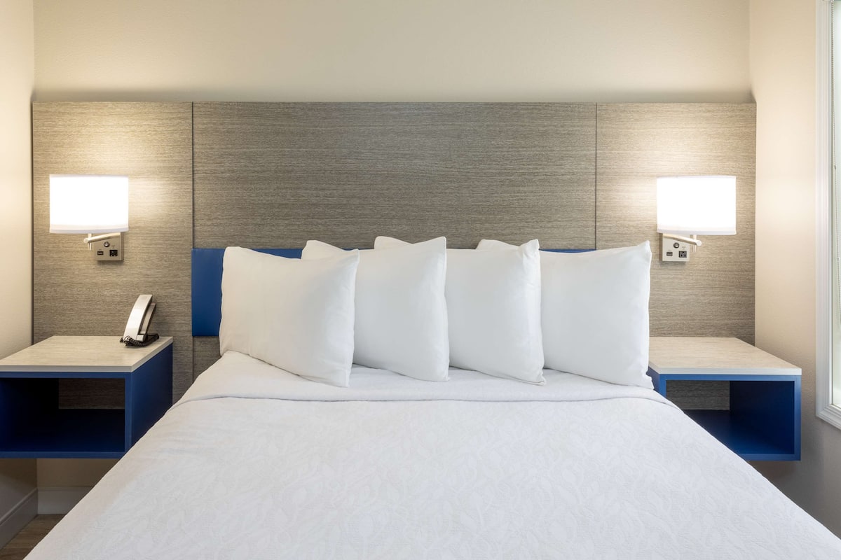 Camera d'albergo con un letto grande, due comodini e una mensola con un telefono, illuminata da lampade a parete.