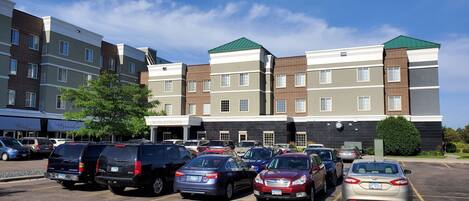 A hotel with multiple floors, a parking lot with various cars, and a clear blue sky.