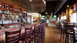 Zona de bar con varios taburetes de madera y una barra larga repleta de botellas.