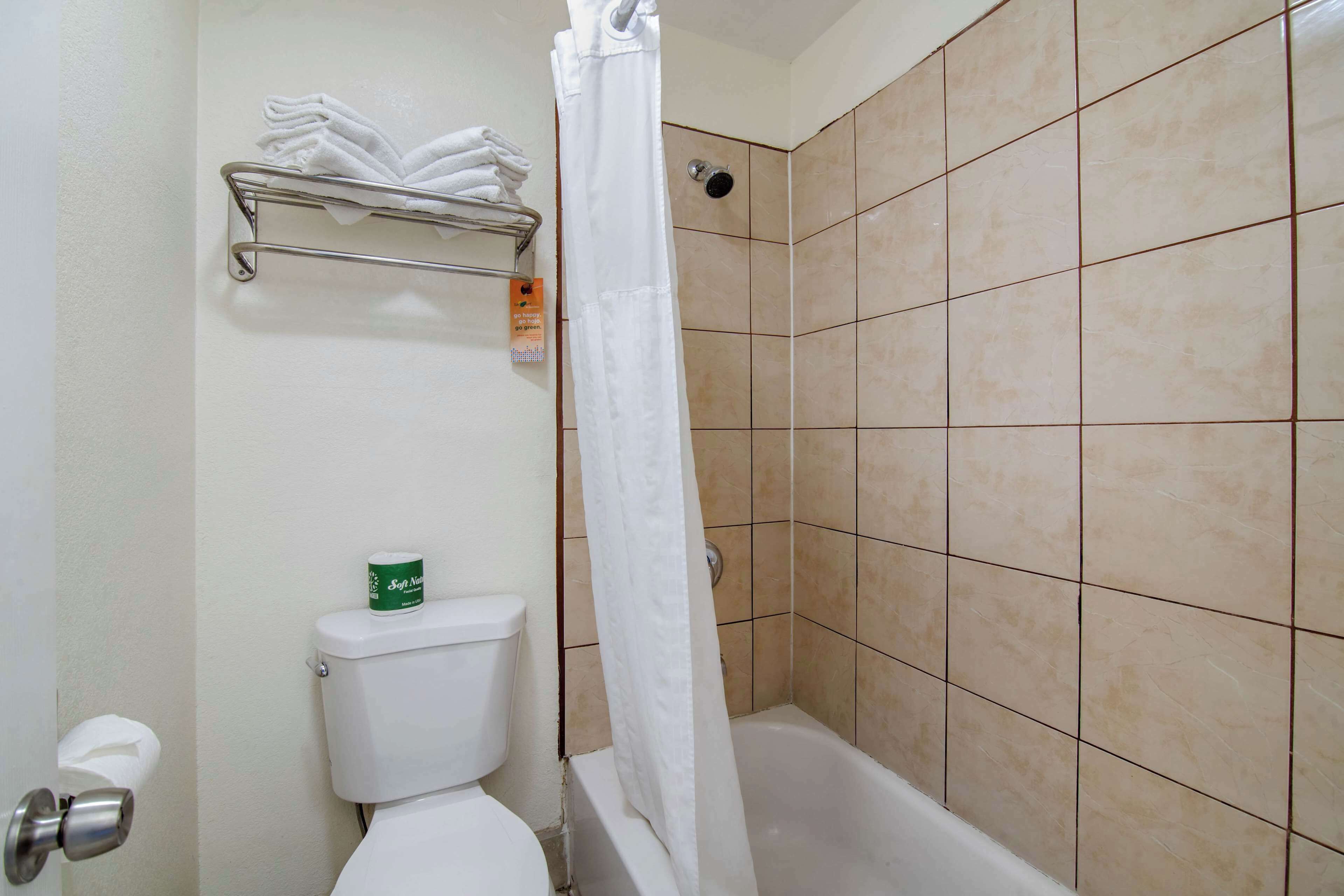 Un baño con inodoro, ducha con cortina y estante con toallas dobladas.