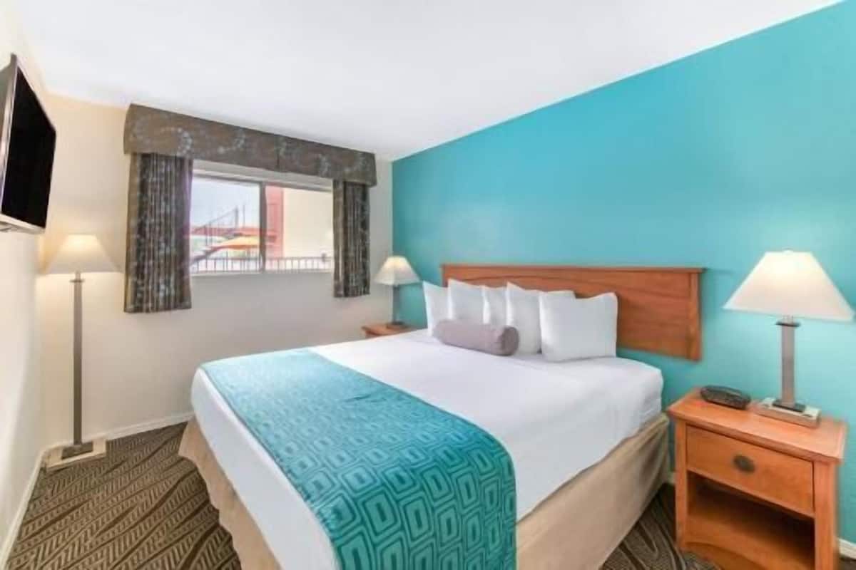 Ein Hotelzimmer mit einem Bett, zwei Nachttischen, einem an der Wand montierten Fernseher und einem Fenster mit Vorhängen.