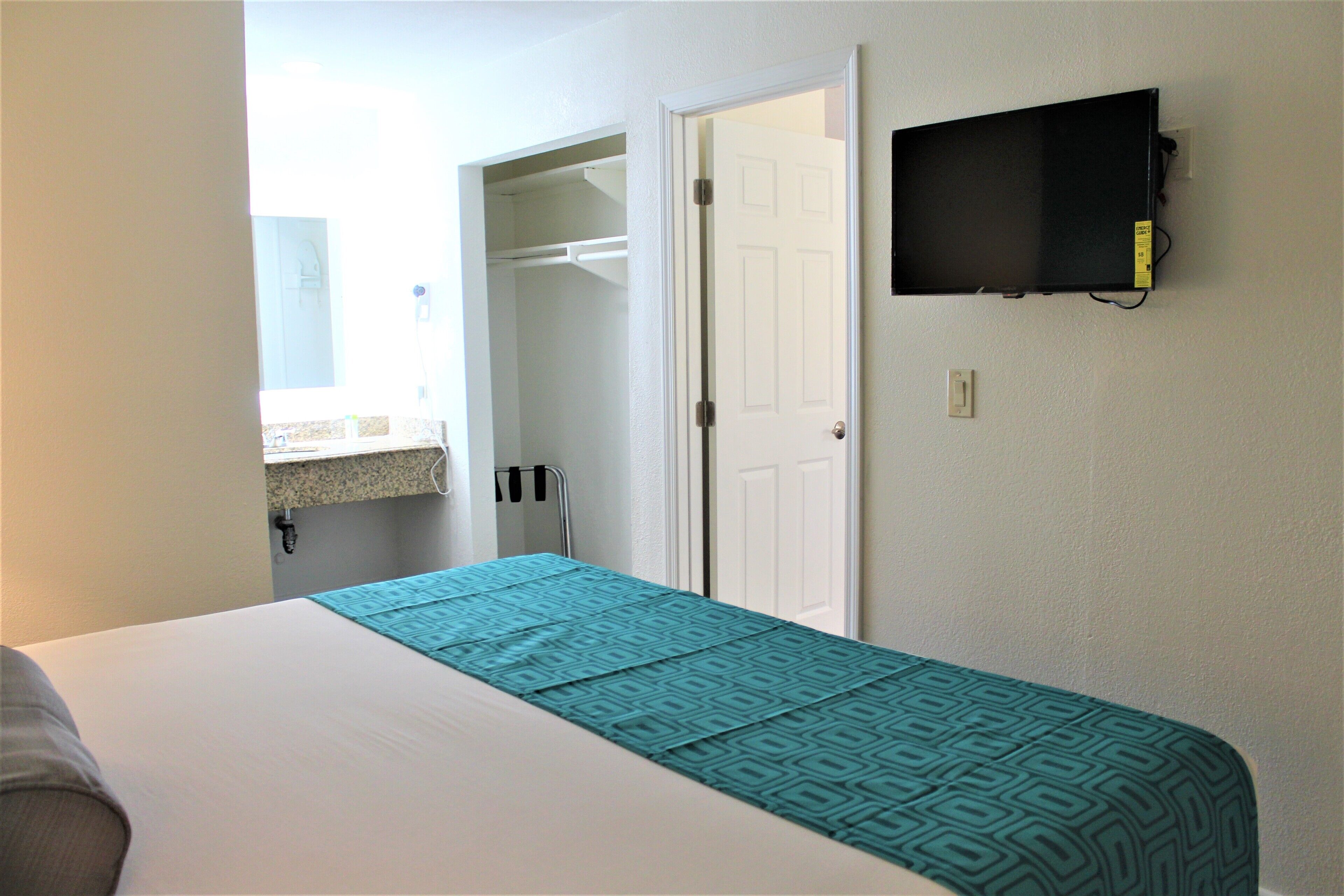 A hotel room with a bed, a TV mounted on the wall, a closet, and a bathroom visible through an open door.