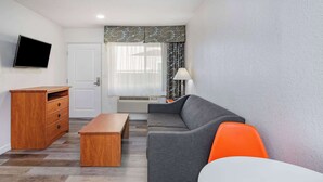 Una sala de estar moderna con un sofá gris, un sillón naranja, un mueble de madera y un televisor de pantalla plana montado en la pared.