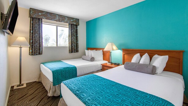 Una habitación de hotel con dos camas, un televisor montado en la pared y una ventana con cortinas.