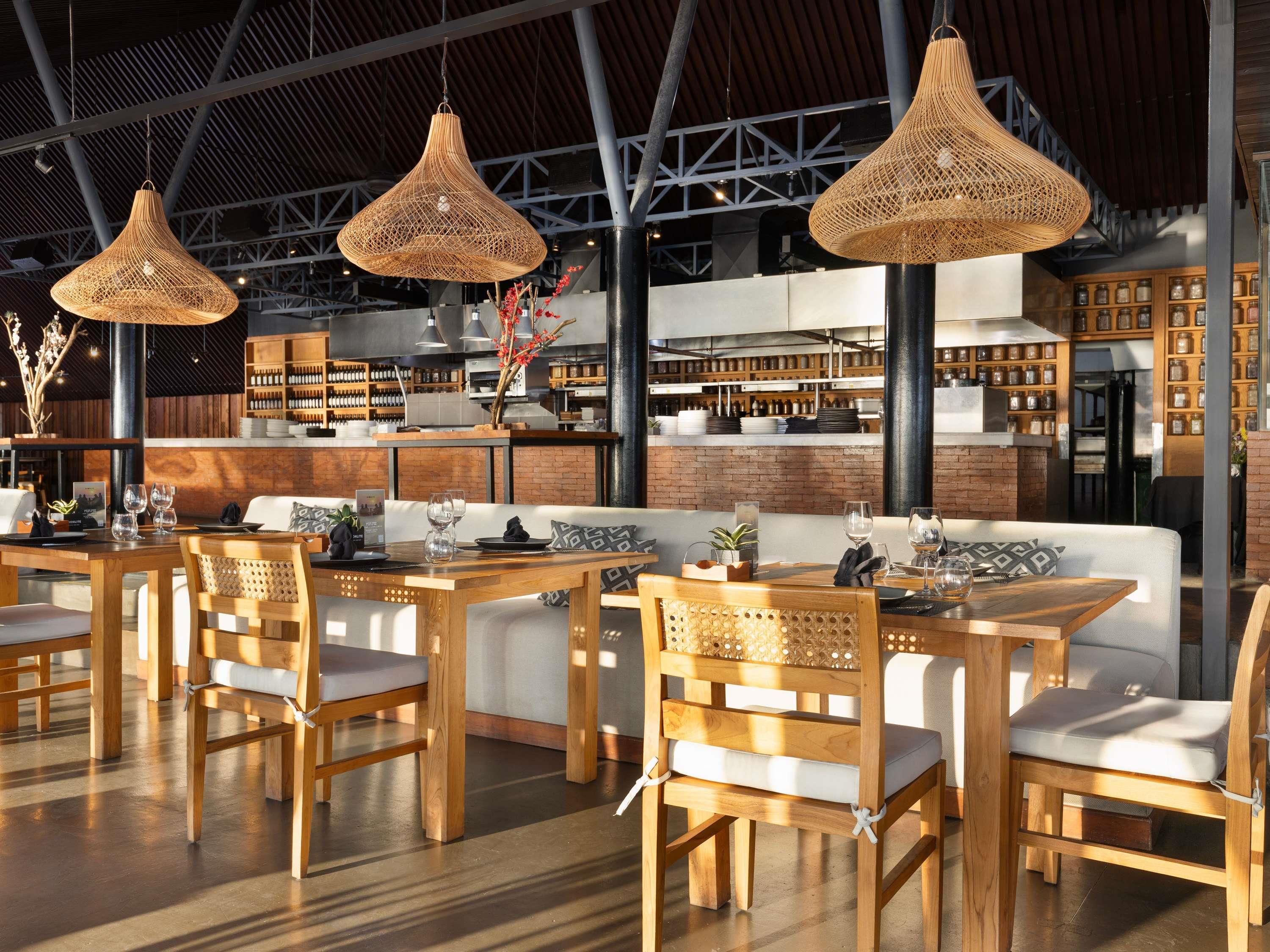 Een restaurantinterieur met houten tafels en stoelen, hangende rieten lampen en een achtergrond van bakstenen muren.