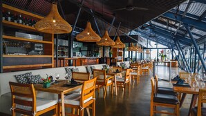A restaurant with wooden furniture, hanging wicker lamps, and a high ceiling with skylights.