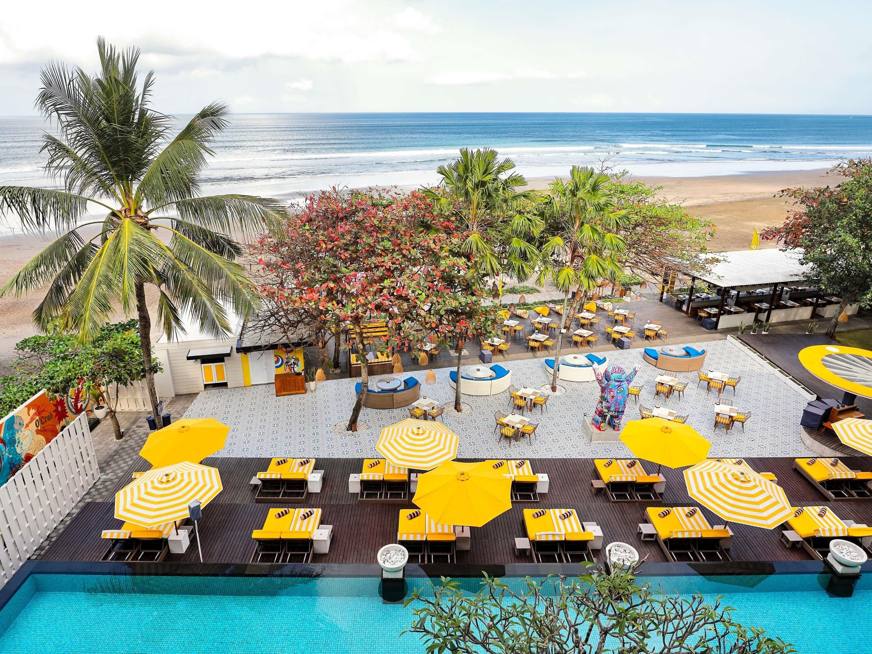 A poolside area with lounge chairs and umbrellas, a beach view, and a tropical setting.
