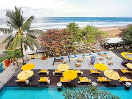 A poolside area with lounge chairs and umbrellas, a beach view, and a tropical setting.