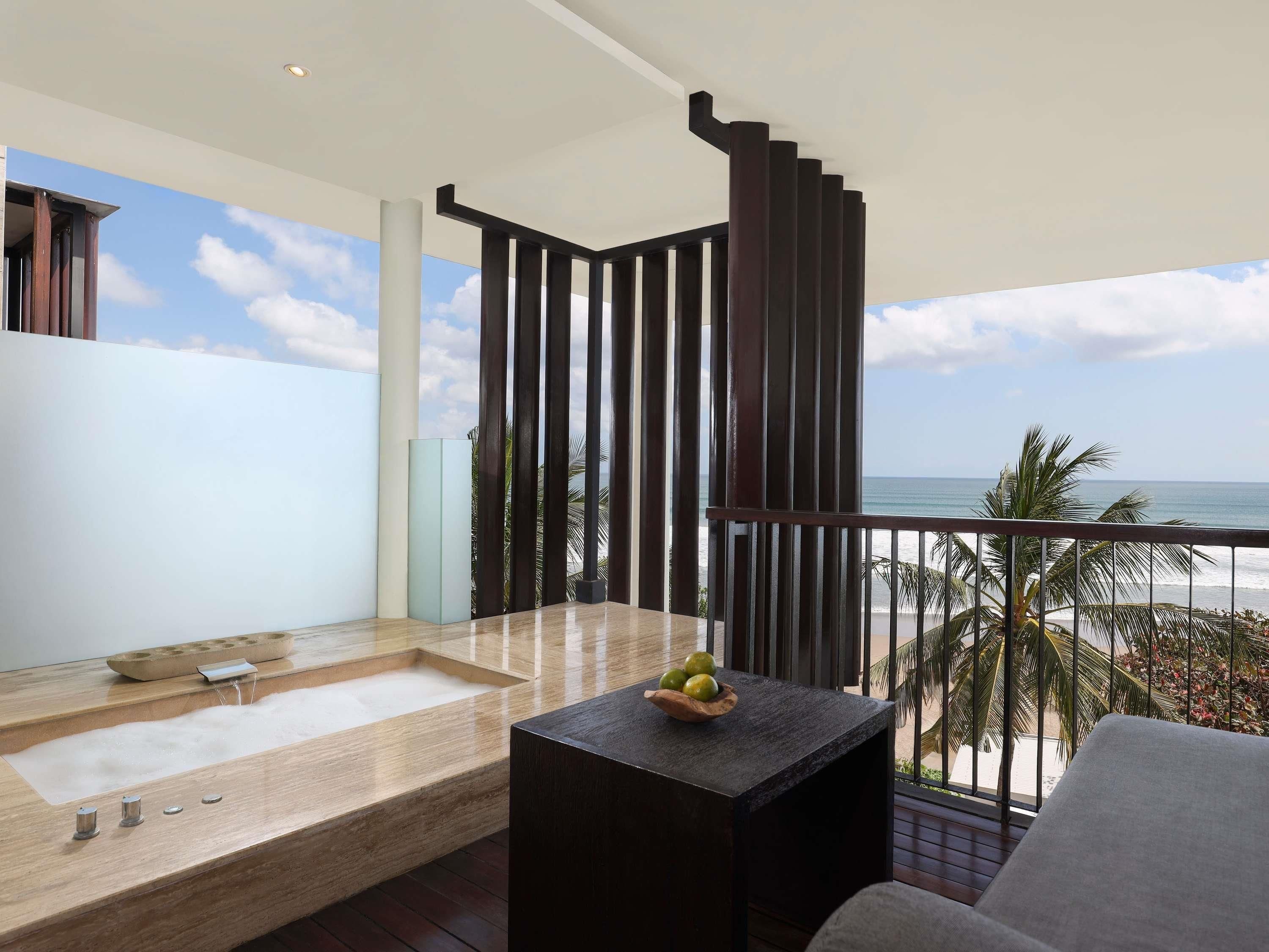 Ein Balkon mit Blick auf den Ozean, ein Holztisch mit Obst und ein Wellnessbereich mit Badewanne.