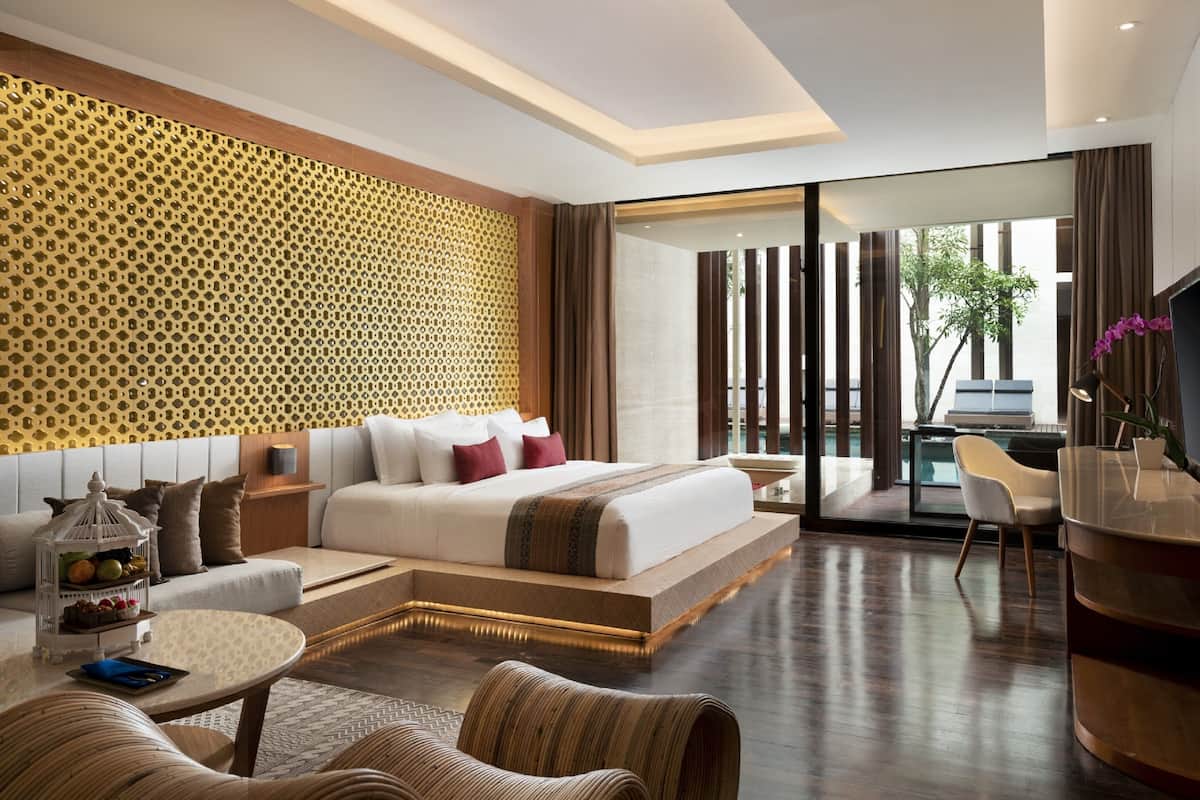 A modern hotel room with a large bed, a seating area with a sofa and chairs, a small table, and a view of the pool and outdoors.