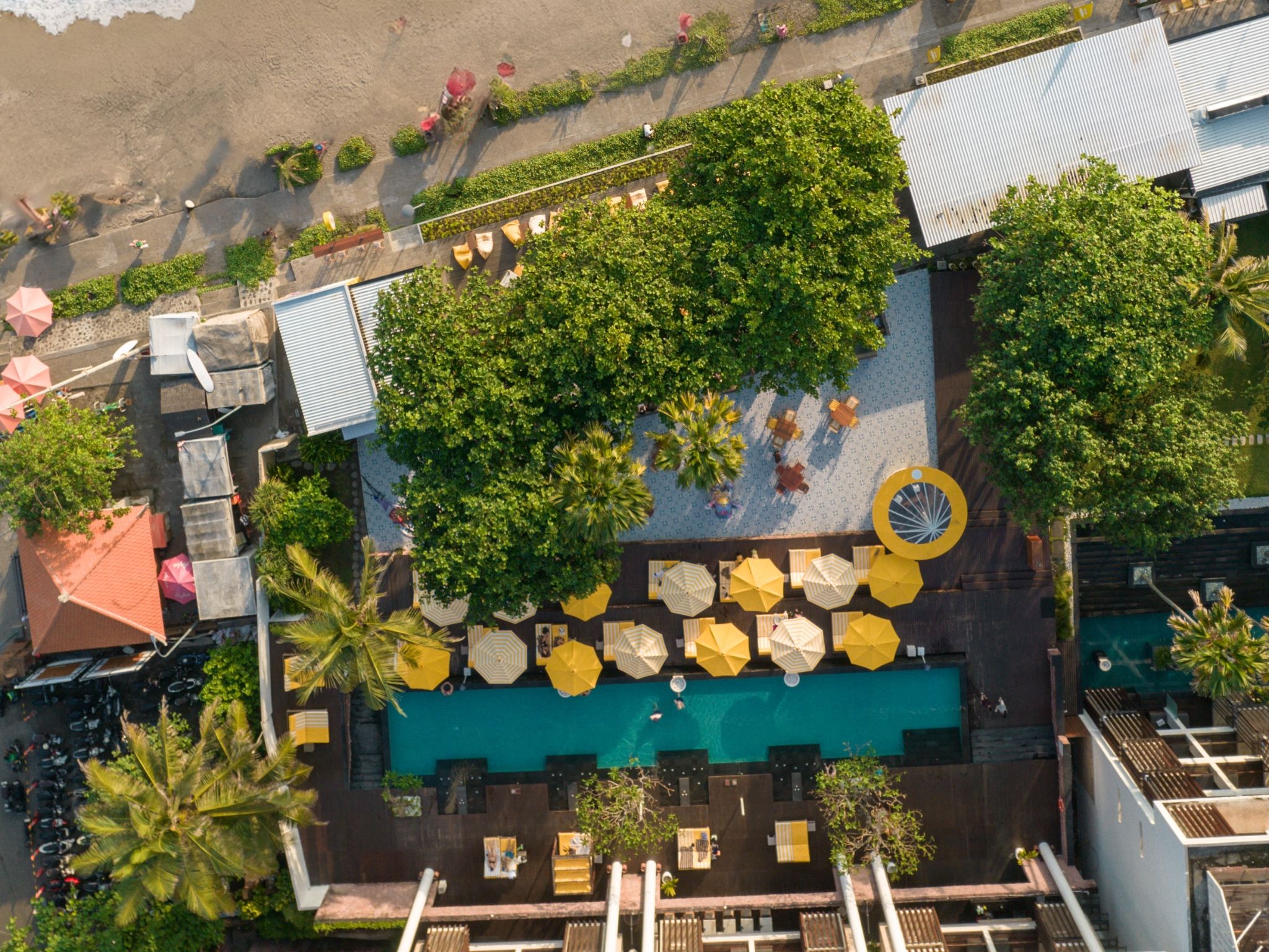 Vista aérea de un área de piscina en azotea con múltiples sombrillas, asientos y un elemento acuático circular.