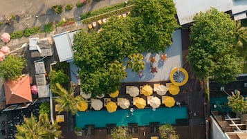Vista aérea de un área de piscina en azotea con múltiples sombrillas, asientos y un elemento acuático circular.