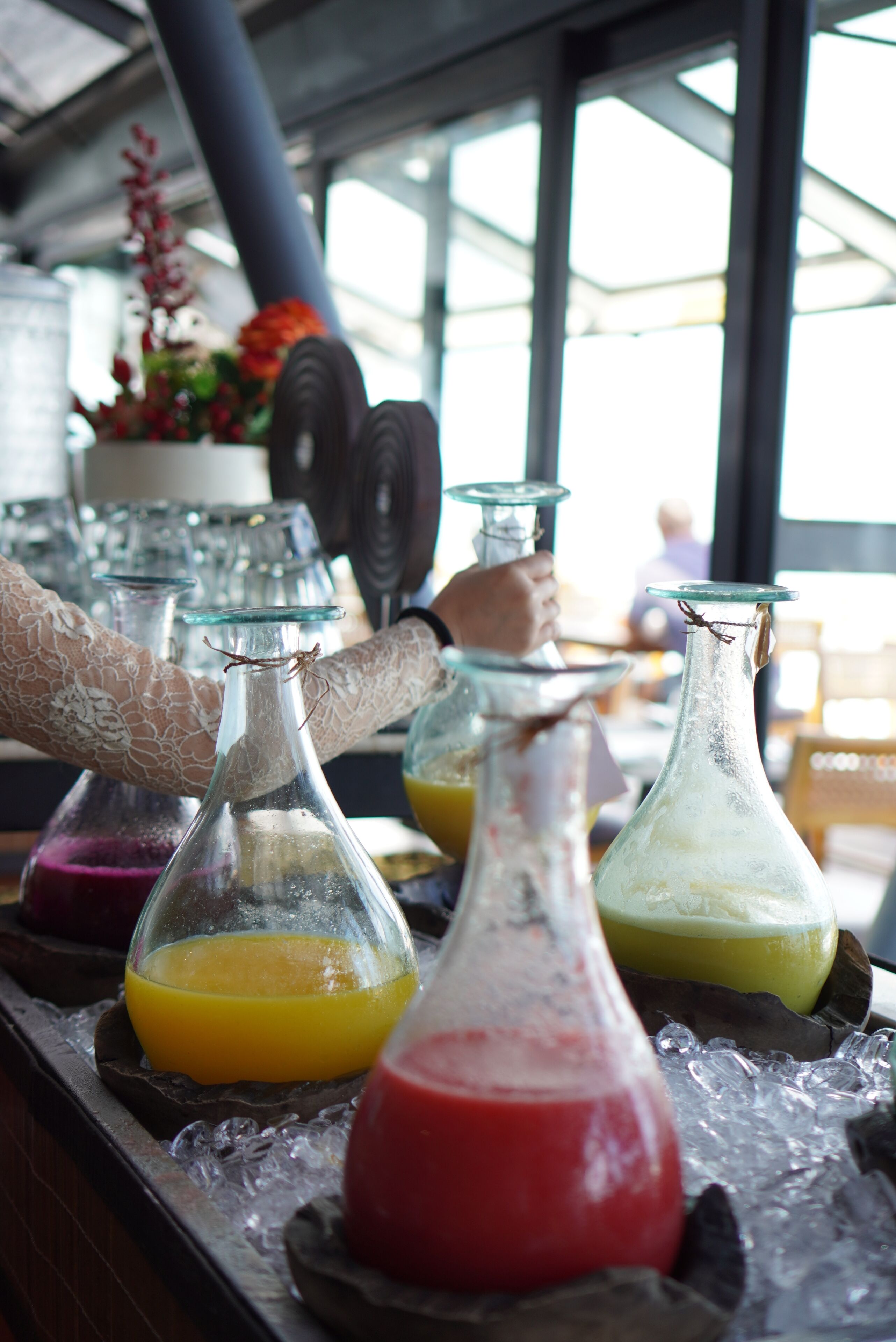 A bar area with multiple glass bottles containing colorful drinks, ice, and a decorative plant in the background.