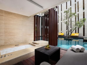 A modern spa area with a wooden floor, a hot tub, a small table with fruit, and a pool with yellow loungers.