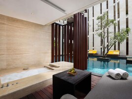 Un área de spa moderna con suelo de madera, una bañera de hidromasaje, una mesita con fruta y una piscina con tumbonas amarillas.