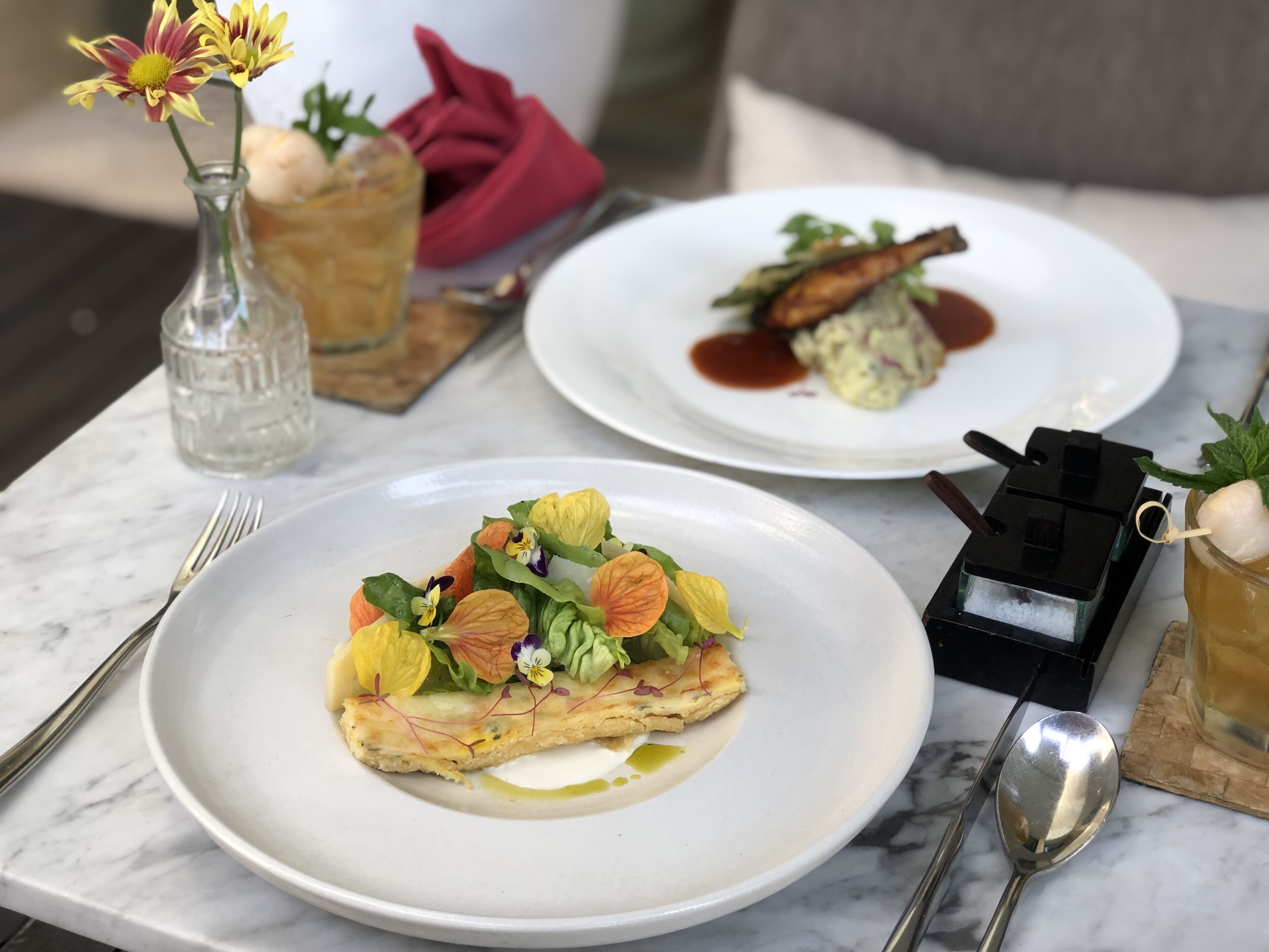 Une table à manger avec deux assiettes de nourriture, un verre et un petit vase avec des fleurs.