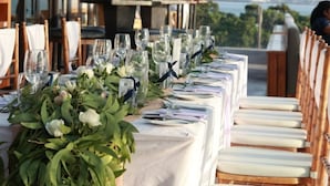 A long dining table set with white tablecloths, glassware, and a floral centerpiece.